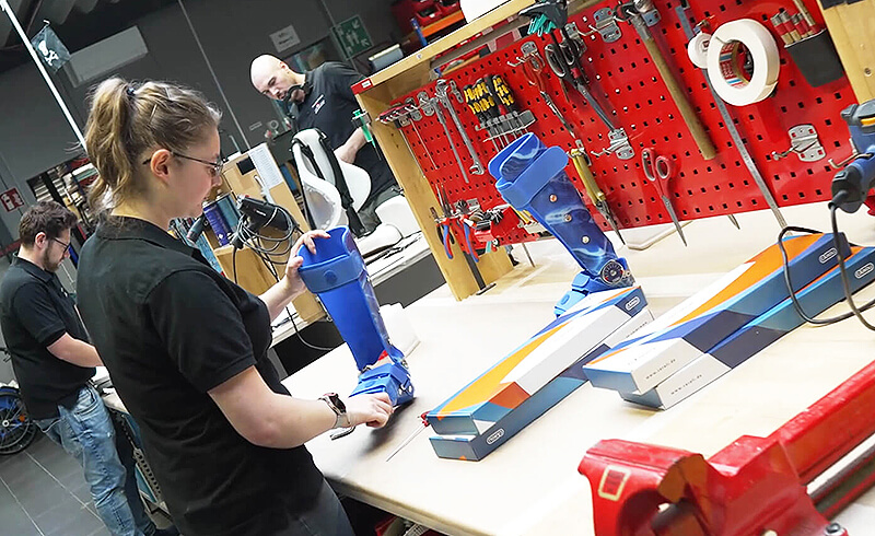 Orthopädietechnikerin montiert eine individuell angepasste Unterschenkelorthese in der Werkstatt an einem Arbeitstisch mit Werkzeugwand